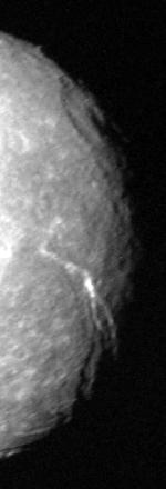A black and white image of the right half of a round spherical body illuminated by the Sun. The terminator runs along the right edge. A large crater with a central pit can be seen at the terminator in the upper half of the image. A large canyon runs from the darkness at the lower-right side to visible center of the body.