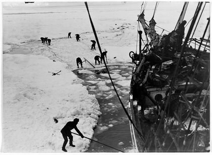 Men with digging tools removing ice surrounding the ship's hull, creating an icy pool of water