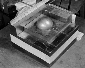 A square base of metal blocks, with a smaller square of metal on the top in the center, a Cooper block (the "core") contained in its center. A ruler along one side of the base shows roughly 10.5 بوصات (270 mm) square.