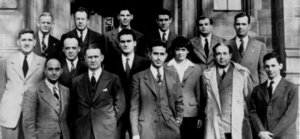 A group of people in suits standing in three rows on the steps in front of a stone building