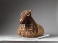 Only one horn is preserved: it is made of linen, papyrus, and several linen bandages, which were then further covered with bandages in an alternating pattern. The other horn has broken off, as the ears. Details of the muzzle are appliquéd or painted on the brown background, and a piece of textile, also brown, with self-bands can be seen.[35]
