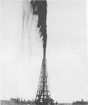 Black-and-white photograph of an oil gusher derrick with a gusher of oil shooting from the top